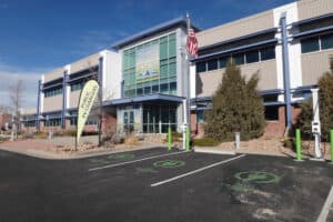 A modern office building with "The Cargo Quip Center" sign. An American flag is displayed, and there are electric vehicle charging stations in front, marked with green symbols on the asphalt.