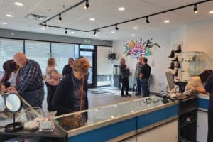 People are inside a store with jewelry displays. Some are examining items, while others are conversing near a mural on the wall.