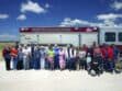 A group of people poses for a photo in front of a Falcon Fire Protection District fire truck on a sunny day.
