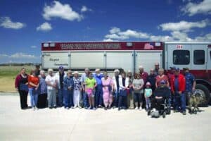 A group of people poses for a photo in front of a Falcon Fire Protection District fire truck on a sunny day.