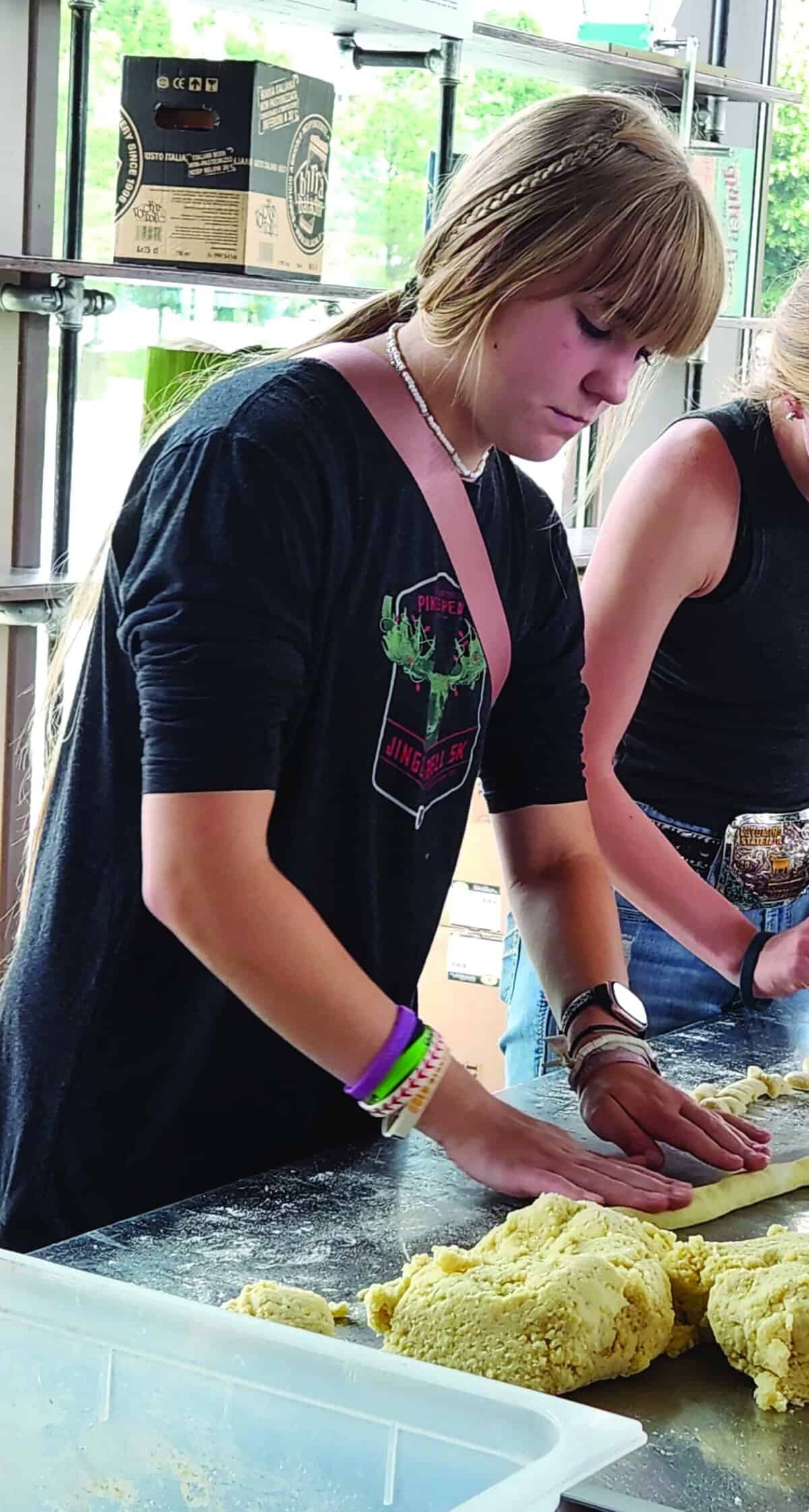 Two people are standing at a counter, pressing and shaping dough with their hands.