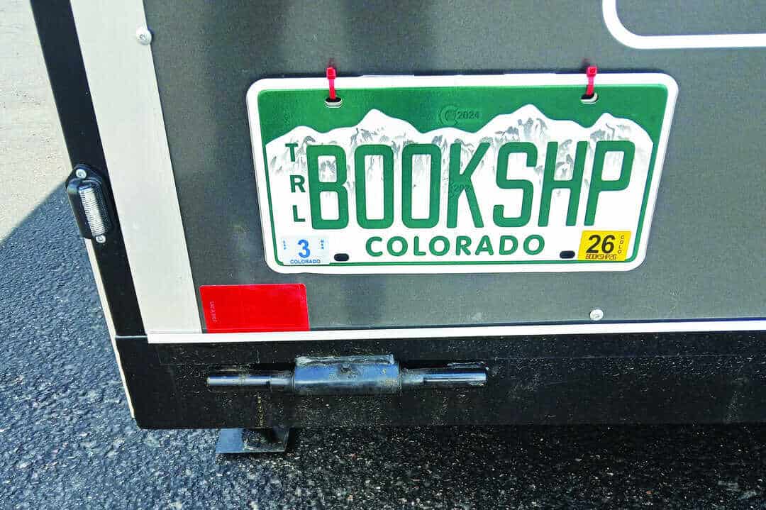 A Colorado license plate on a vehicle reads "BOOKSHP" in green letters, with white mountains in the background.