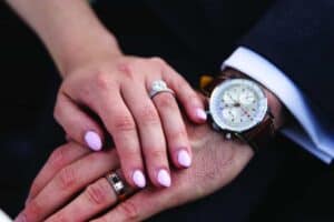 A close-up of two hands resting on each other, both wearing rings; the person on the right also wears a watch with a brown leather strap.