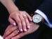 A close-up of two hands resting on each other, both wearing rings; the person on the right also wears a watch with a brown leather strap.
