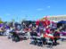 People sit at tables and gather around food trucks at an outdoor food festival on a sunny day with clear skies.