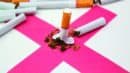 A broken cigarette lies on a pink X with tobacco scattered, surrounded by unbroken cigarettes.