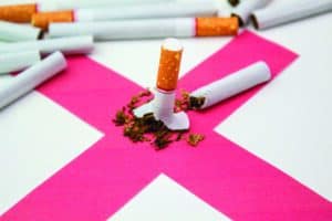 A broken cigarette lies on a pink X with tobacco scattered, surrounded by unbroken cigarettes.