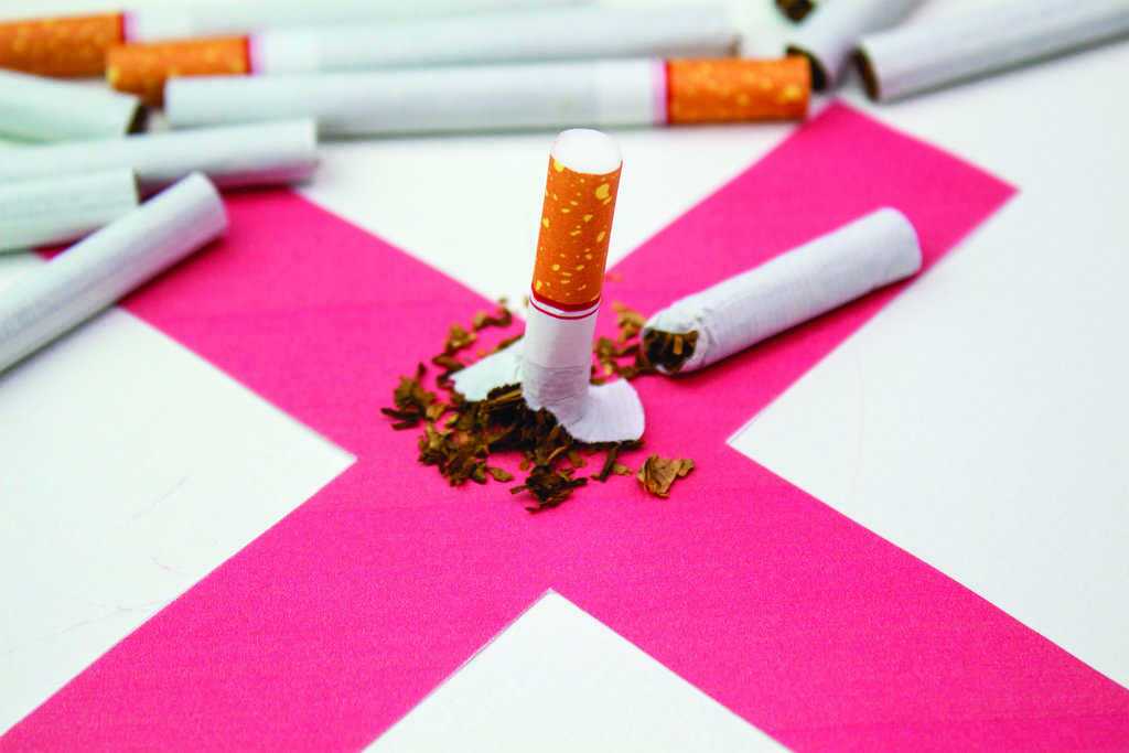 A broken cigarette lies on a pink X with tobacco scattered, surrounded by unbroken cigarettes.