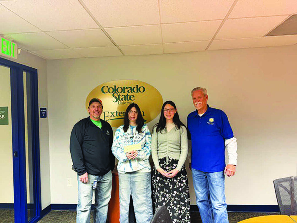 Four people stand indoors in front of a Colorado State University Extension sign, posing for a group photo.