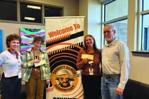Four adults stand indoors in front of a "Welcome to Bennett Ranch Elementary" banner, holding papers and smiling at the camera.