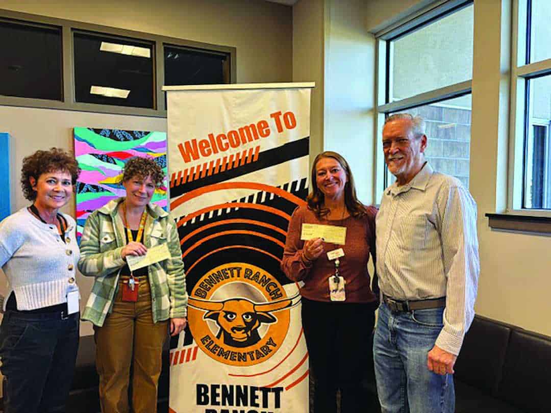 Four adults stand indoors in front of a "Welcome to Bennett Ranch Elementary" banner, holding papers and smiling at the camera.