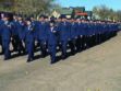 A large group of uniformed military personnel marches in formation on a paved outdoor area under a clear sky.