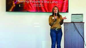 A woman stands at a podium giving a presentation titled "Advancing Food is Medicine: Healing People & the Land" with a FreshRx Oklahoma logo displayed on a screen behind her.