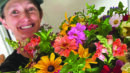 A person wearing a green cap smiles while holding a large, colorful bouquet of assorted flowers in front of a plain background.