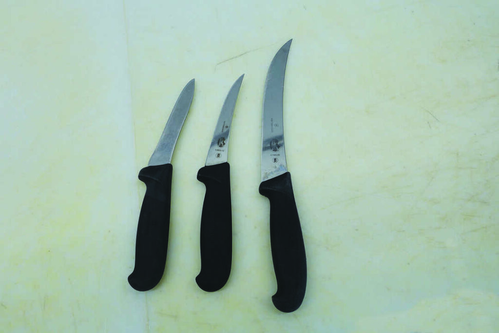 Three boning knives with black handles are arranged side by side on a light-colored, scratched surface.
