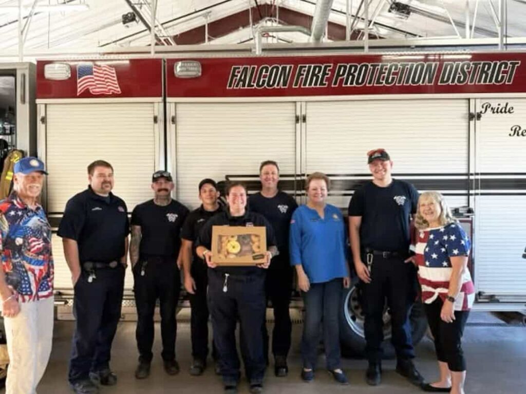 A group of Falcon Fire Protection District firefighters and civilians stand in front of a fire truck.