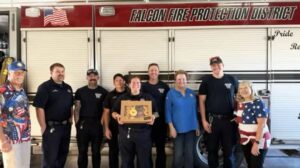A group of Falcon Fire Protection District firefighters and civilians stand in front of a fire truck.