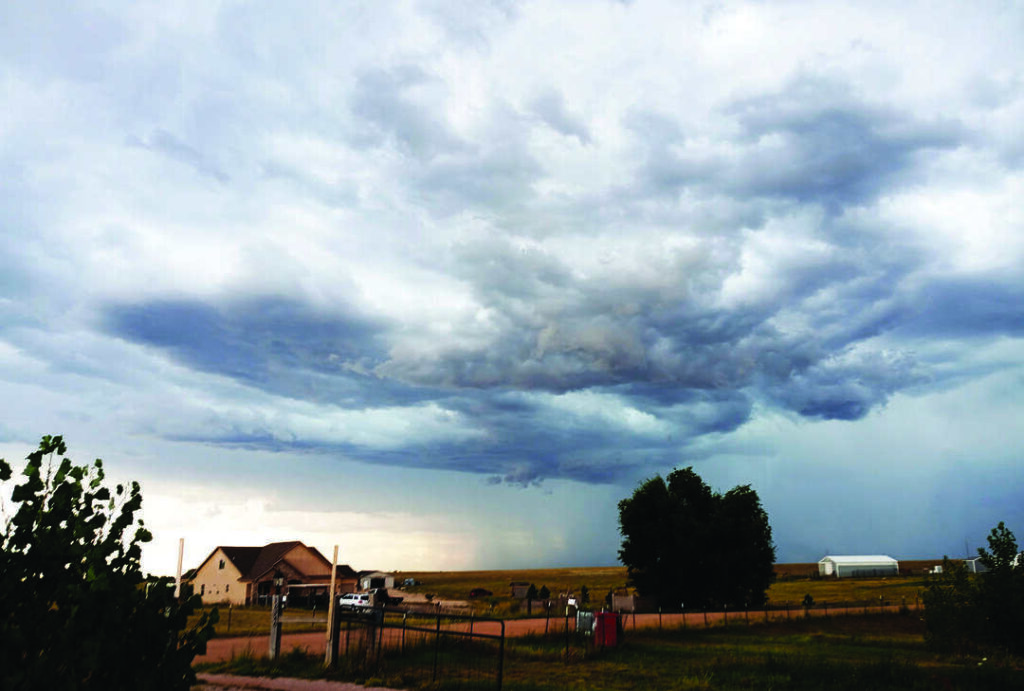 Dark storm clouds gather over a rural landscape with a house and fields.