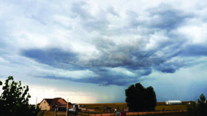 Dark storm clouds gather over a rural landscape with a house and fields.