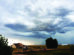 Dark storm clouds gather over a rural landscape with a house and fields.
